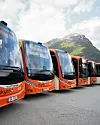 Oransje Yutong-bussar frå Firda Billag Buss og Skyss står på rekke framfor fjellandskap.
